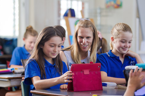 Students working on tablet devices with teacher
